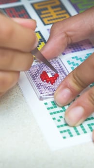 Human creating a picture by using tweezers, transparent baseplate and colorful pixel squares