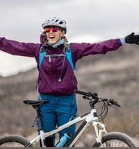 a young woman standing in front of her mountain bike with her arms outstretched