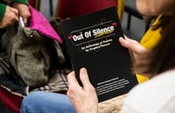 a person holding a book with black cover and white text decorated with colourful doodles