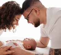 photo de bébé avec ses parents au dessus de lui et les regarde