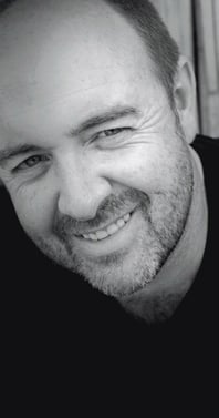 Portrait of Martin Osner, South African artist and photographic artist, smiling in black and white