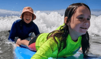 a woman guiding a young girl on a surfboard