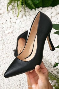 a woman's hand holding a black pointed toe high heeled shoes