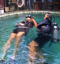 a dive master and student in scuba gear in a pool  geting the introduction dive course