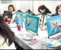 paint party women sitting at a table with art work