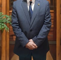 Major General Ayman Syedelahl stands wearing an elegant grey suit, with luxurious office decor 