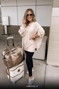 a woman in a white sweater and black leggings and a suitcase