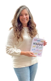 pretty woman in jeans and a white sweater with long brown hair and a smile, holding a book