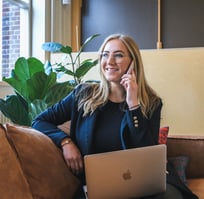 Mulher sorrindo enquanto fala ao telefone, com um laptop no colo.