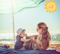 a woman sitting on a blanket with her baby near seaside