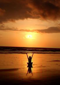 a person standing on a beach with a person holding a kite
