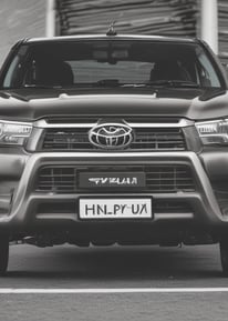 A close-up view of the front portion of a vintage Toyota vehicle. The image highlights the prominent grille with the Toyota logo in the center. There is a cloth draped over part of the grille and headlights, suggesting storage or protection.