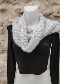 Tour de cou tricoté à la main posé sur un mannequin blanc habillé d'un haut noir