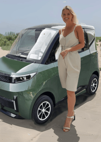 middle age woman poses with dark green Impulse Electromotive Nano-3 Micro EV car