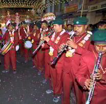 A team of Manohar Brass Band musicians aligned and playing clarinet, thap dhol, and nagara drum instruments.