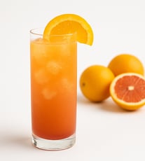 Orange drink with ice cubes and oranges in the background