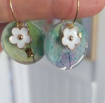 a person holding a pair of earrings with flowers