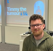 A photo of Chandy . In the background is a presentation with 'Timmy The Tumour & Me'.