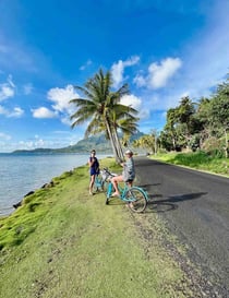 Eva and Manon cycling on a palm-lined road in Bora Bora, French Polynesia.