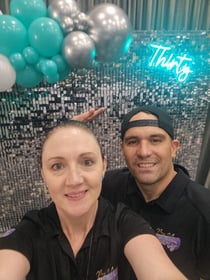 Carly and Kahn from SweetAz Co. taking a selfie in front of the silver shimmer wall, Thirty neon sign, and balloon garland fo