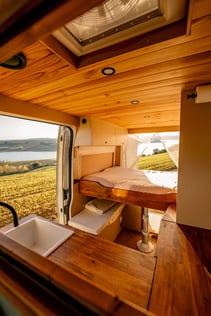 Intérieur d’un van aménagé chaleureux , l’extérieur est visible on peut voir un lac