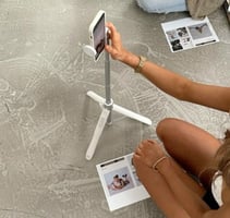 Woman filming content with a phone on a tripod and printed materials on the floor.