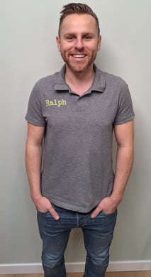 een man in een grijs shirt en broek die voor een muur staat
