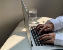 Hands typing on a laptop next to a glass of water in a minimal workspace.