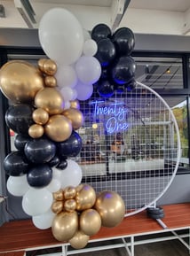 White circle mesh backdrop with blue Twenty One neon sign and a gold, black and white balloon garland, Redlands