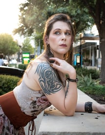 woman leaning on cement wall wearing flower dres with sunset behind her looking wistfully behind her