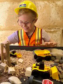Smiling child in a construction outfit playing with a sensory construction site small world play.