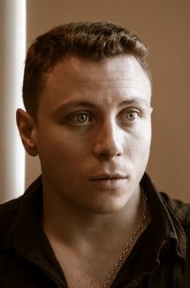 A sepia portrait of a handsome blue-eyed young man lit form one side and looking straight ahead