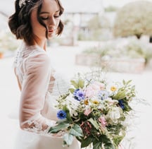Jeune femme le jour de son mariage dans une robe blanche entrain de tenir un bouquet de fleurs
