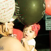 baby with red hair bow being held by father in the middle of a sea of balloons