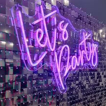 Glowing pink Let's Party neon sign on a silver shimmer wall for an event in Brisbane.