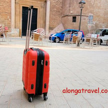 A small red carry-on standing in the middle of a square shows an ease of moving when packed light 