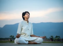 a woman sitting on a mat mat in a field doing meditation