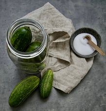 a jar of small cucumbers with a bowl of salt and a linen cloth