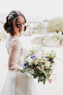 Jeune femme le jour de son mariage dans une robe blanche entrain de tenir un bouquet de fleurs