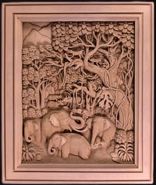 Intricate teak carving of elephants and deer in a lush jungle scene, showcasing Thai artistry.