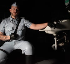 man dressed in leather squatting in low light beside sink