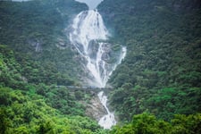 A water fall in middle of mountains and rocks with greenery surrounding