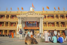 A temple complex with people standing outside the temple and flags at the top of the temple.