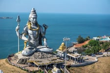 Lord Shiva statue with the background of blue sea, trees beside the status