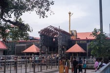 A temple entrance build in red color rocks with people standing in front of the temple.