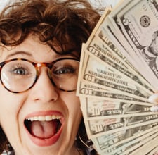 a woman with glasses and a blue shirt holding a stack of money