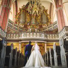Brautpaar in einer Kirche vor einem kunstvoll geschmückten Altar.