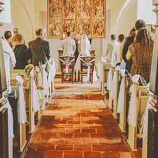 Die Ansicht einer Hochzeitszeremonie von hinten in einer Kirche. Die Braut und der Bräutigam stehen vor dem Altar und den Kir