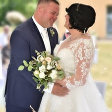  Das Bild zeigt ein lächelndes Brautpaar, das sich während der Hochzeitszeremonie liebevoll ansieht. Die Braut trägt ein weiß