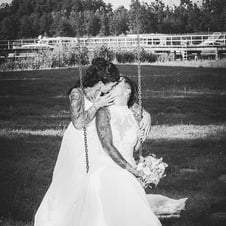 Verliebtes Brautpaar in weißen Hochzeitskleidern, umgeben von Natur.